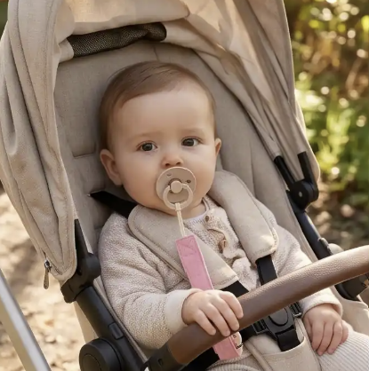 Bebe dans la poussette au parc avec l'attache tetines rose 